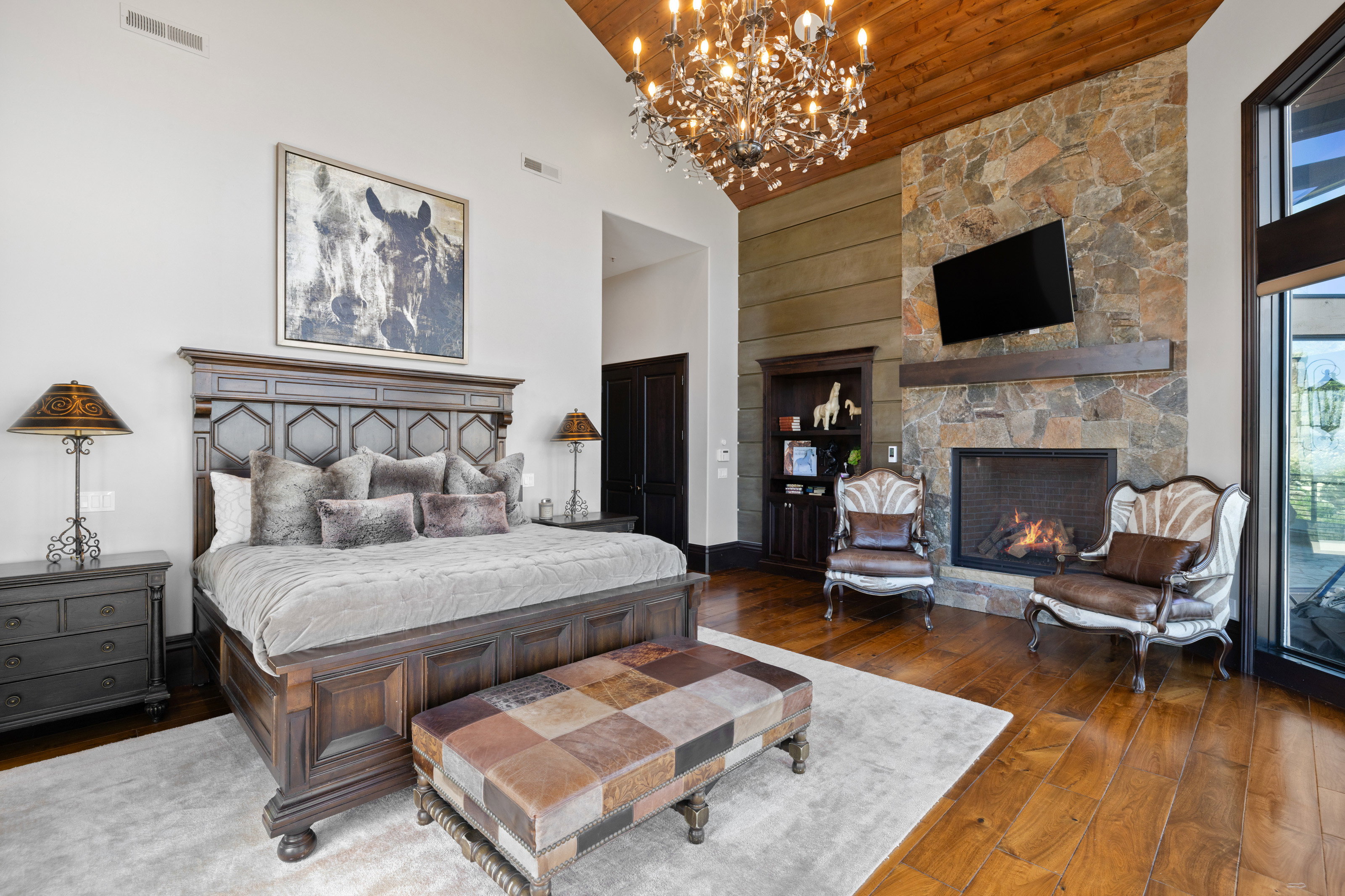 Bedroom with high vaulted ceiling, dark wood-type flooring, wooden ceiling, a stone fireplace, and a chandelier