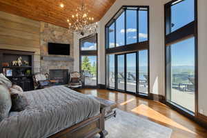 Bedroom featuring wooden ceiling, high vaulted ceiling, hardwood / wood-style flooring, access to outside, and a stone fireplace
