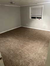 Empty room featuring a textured ceiling, dark colored carpet, and ornamental molding