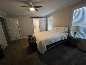 Bedroom featuring ornamental molding, a barn door, ensuite bathroom, dark carpet, and ceiling fan