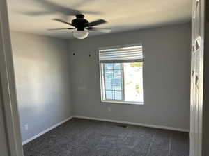 Unfurnished room with dark colored carpet and ceiling fan