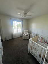 Carpeted bedroom with a crib and a ceiling fan