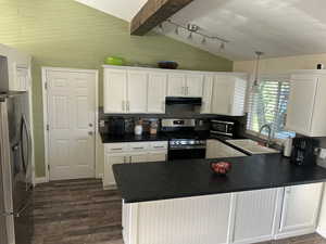 Kitchen with appliances with stainless steel finishes, dark countertops, white cabinetry, dark wood-type flooring, and wood walls