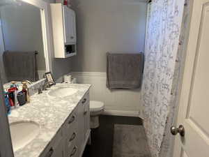 Full bathroom featuring double vanity, wainscoting, and a shower with curtain