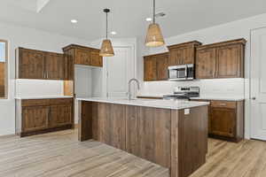 Kitchen featuring wood tiled floors, pendant lighting, appliances with stainless steel finishes, a center island with sink, and recessed lighting