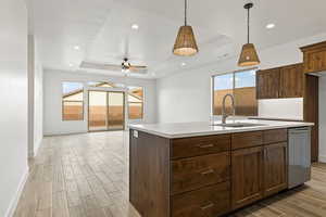 Kitchen featuring a tray ceiling, wood finish floors, an island with sink, decorative light fixtures, and dishwasher