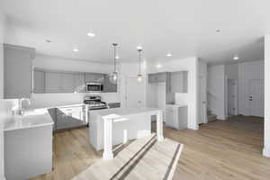 Kitchen with gray cabinets, a kitchen island, hanging light fixtures, light wood finished floors, and recessed lighting