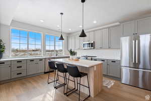 Kitchen with gray cabinetry, stainless steel appliances, a kitchen island, light stone countertops, and a breakfast bar area