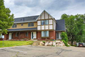 Tudor home featuring a shingled roof, uncovered parking, brick siding, and stucco siding