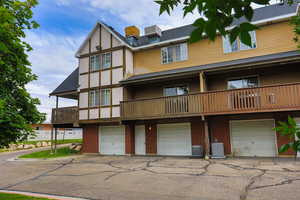 Rear view of property featuring a garage, a balcony, brick siding, and driveway