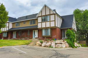 Tudor-style house featuring uncovered parking, brick siding, a shingled roof, and stucco siding