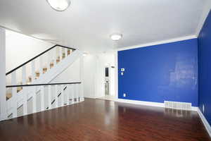 Unfurnished living room featuring dark wood-style floors, crown molding, and stairway