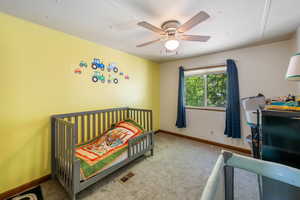Carpeted bedroom with a ceiling fan and a nursery area