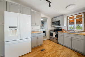 Kitchen featuring gray cabinetry, wooden counters, stainless steel appliances, light wood-type flooring, and vaulted ceiling