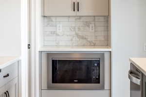 Detailed view of appliances with stainless steel finishes, backsplash, and white cabinets