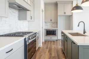 Kitchen featuring appliances with stainless steel finishes, custom range hood, light wood-type flooring, backsplash, and hanging light fixtures