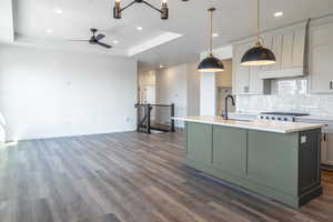 Kitchen featuring green cabinets, backsplash, a center island with sink, a raised ceiling, and dark wood-style floors