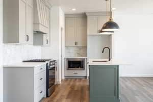 Kitchen featuring appliances with stainless steel finishes, green cabinets, light stone countertops, a kitchen island with sink, and custom range hood