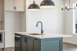 Kitchen with decorative light fixtures, dark wood-type flooring, an island with sink, light stone counters, and a chandelier