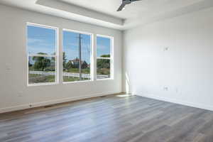Empty room with wood finished floors, a tray ceiling, and a ceiling fan