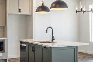 Kitchen with dark wood finished floors, pendant lighting, light stone countertops, a center island with sink, and gray cabinetry