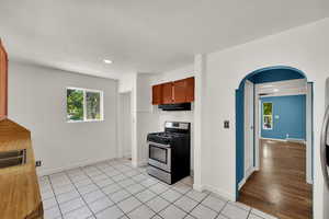 Kitchen with arched walkways, stainless steel gas range oven, light tile patterned floors, light countertops, and brown cabinets