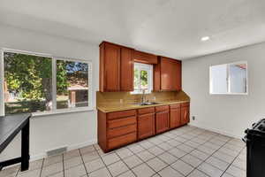 Kitchen with light countertops, brown cabinets, gas stove, light tile patterned floors, and tasteful backsplash