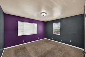 Carpeted spare room featuring a textured ceiling and baseboards