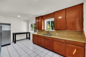 Kitchen featuring tasteful backsplash, brown cabinetry, light countertops, freestanding refrigerator, and light tile patterned floors