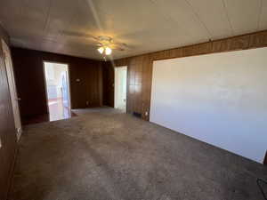 Unfurnished room featuring carpet, wooden walls, and ceiling fan