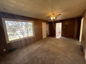 Carpeted spare room featuring wooden walls and a ceiling fan