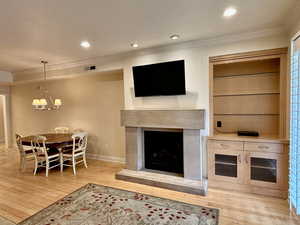 Living area featuring crown molding, a premium fireplace, recessed lighting, wood finished floors, and a chandelier
