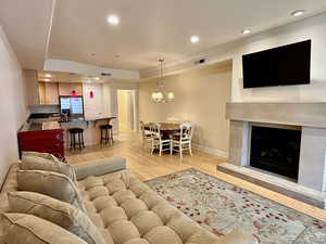 Living room with crown molding, recessed lighting, light wood finished floors, a premium fireplace, and a tray ceiling