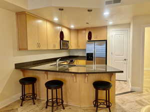 Kitchen featuring a peninsula, appliances with stainless steel finishes, dark stone counters, hanging light fixtures, and a breakfast bar