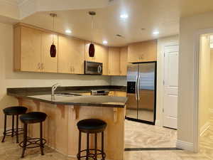Kitchen with hanging light fixtures, a peninsula, appliances with stainless steel finishes, recessed lighting, and a kitchen bar