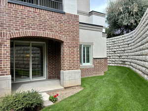 View of exterior entry featuring brick siding, a yard, stucco siding, and a patio