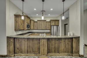 Kitchen with stainless steel appliances, dark stone counters, decorative light fixtures, brown cabinetry, and recessed lighting