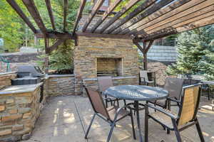 View of patio with outdoor dining space, a pergola, an outdoor stone fireplace, and area for grilling