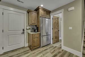 Kitchen with freestanding refrigerator, decorative backsplash, brown cabinets, light wood-style flooring, and recessed lighting