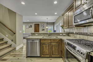 Kitchen with appliances with stainless steel finishes, a peninsula, brown cabinets, recessed lighting, and tasteful backsplash