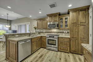 Kitchen featuring backsplash, stainless steel appliances, a peninsula, brown cabinets, and recessed lighting
