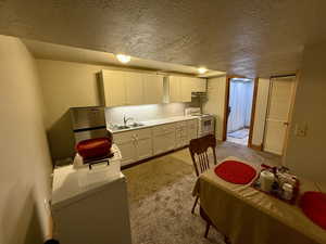 Kitchen with a textured ceiling, electric stove, light countertops, light colored carpet, and white cabinets