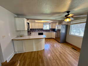 Kitchen featuring stainless steel refrigerator with ice dispenser, a peninsula, light wood finished floors, a textured ceiling, and ceiling fan