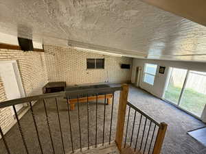 Carpeted living room with brick wall, vaulted ceiling, and a textured ceiling