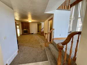 Staircase featuring a textured ceiling, a brick fireplace, and carpet floors