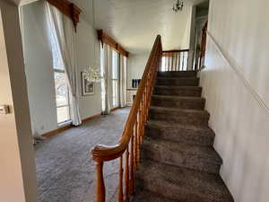 Staircase with a textured ceiling, carpet flooring, and a chandelier