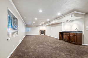 Large family room with crown molding, dark colored carpet, recessed lighting, a fireplace, and a textured ceiling