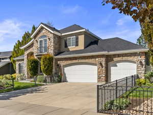 Traditional home featuring stone siding, a fenced front yard, driveway, an attached garage, and roof with shingles