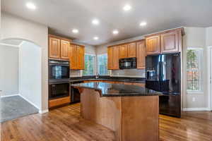 Kitchen with black appliances, dark stone counters, recessed lighting, a center island, and arched walkways
