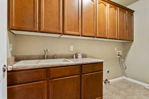 Laundry area with hookup for a washing machine, cabinet space, light tile patterned flooring, and hookup for an electric dryer